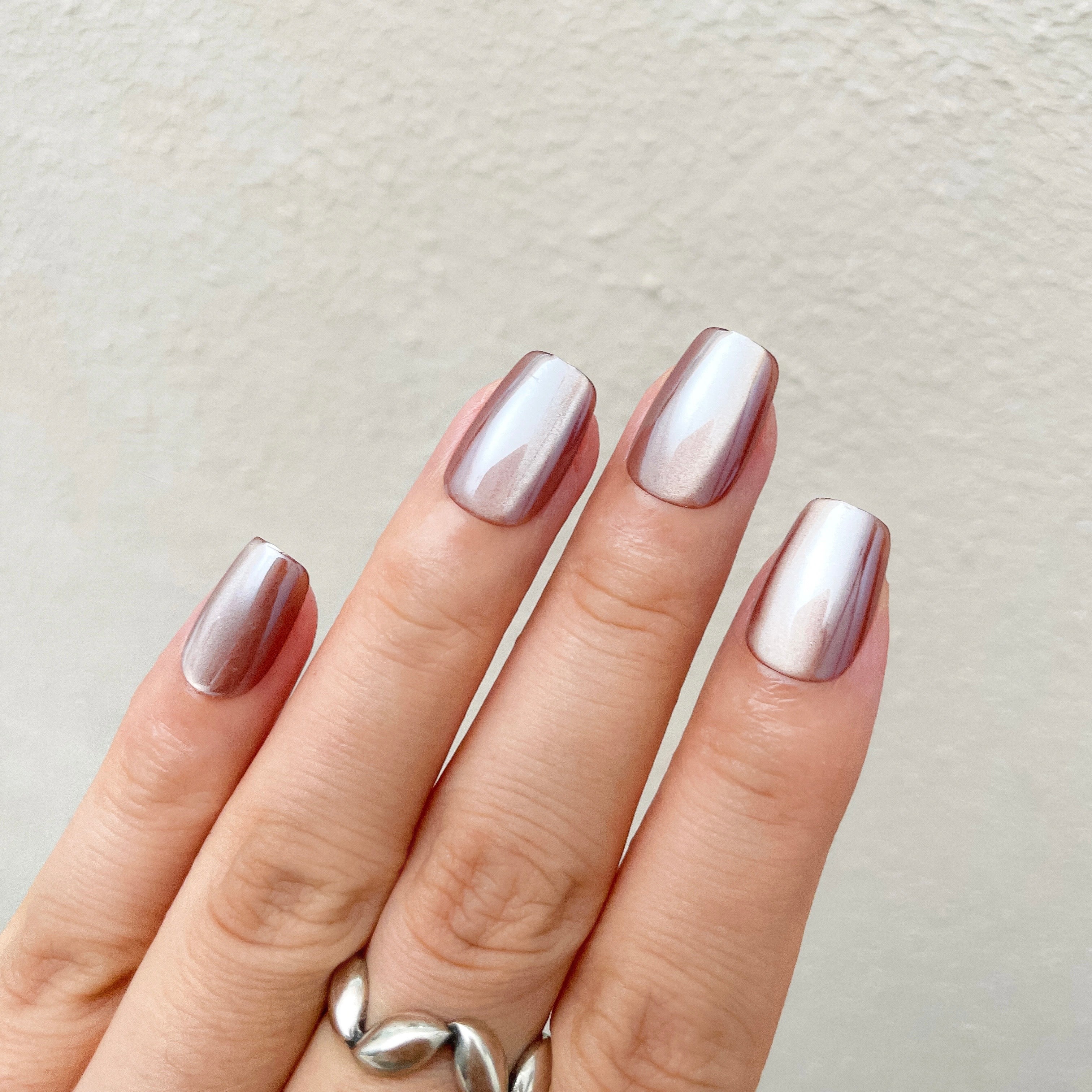 Hand with metallic pink nail polish on a neutral background