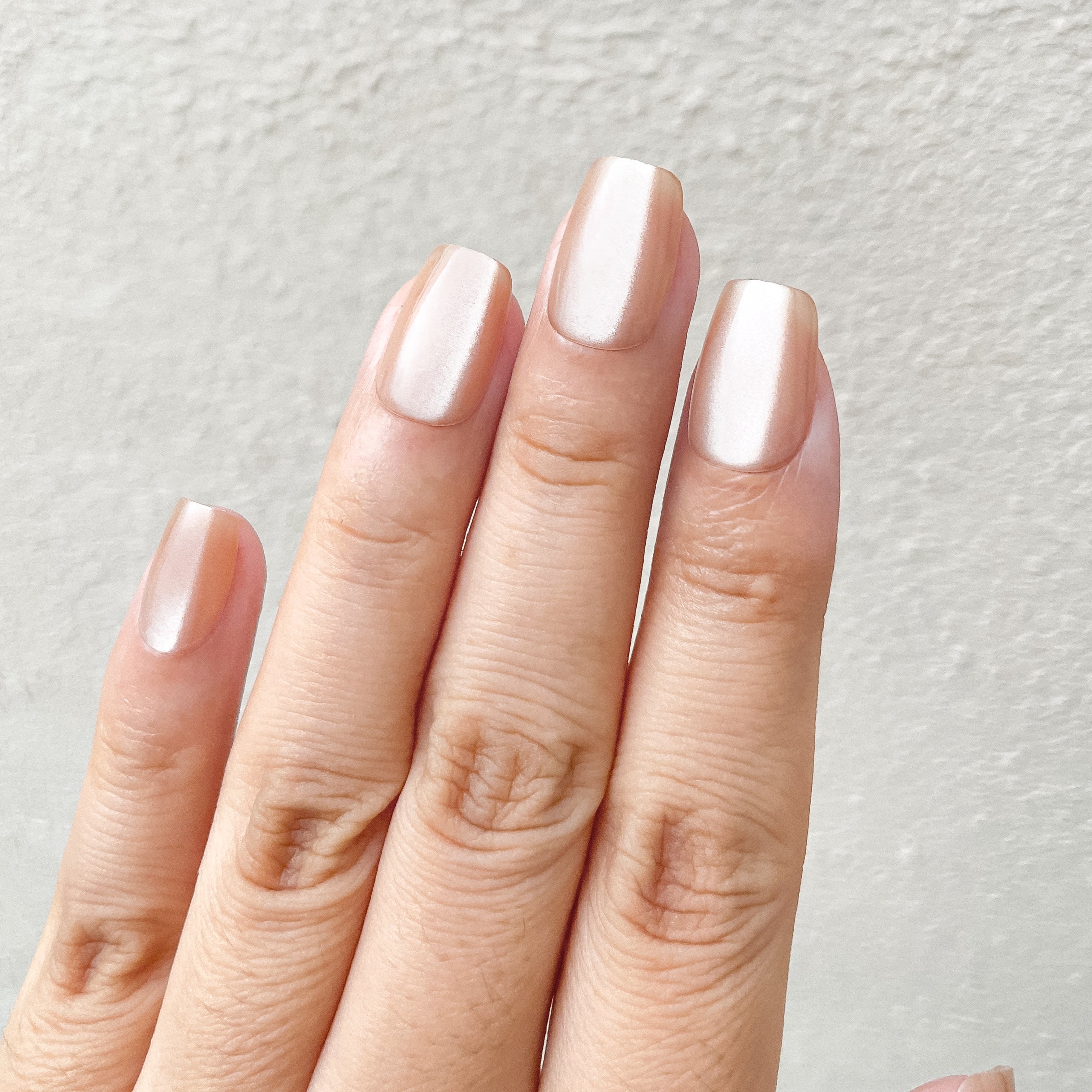 Close-up of a hand with light pink nail polish on a neutral background