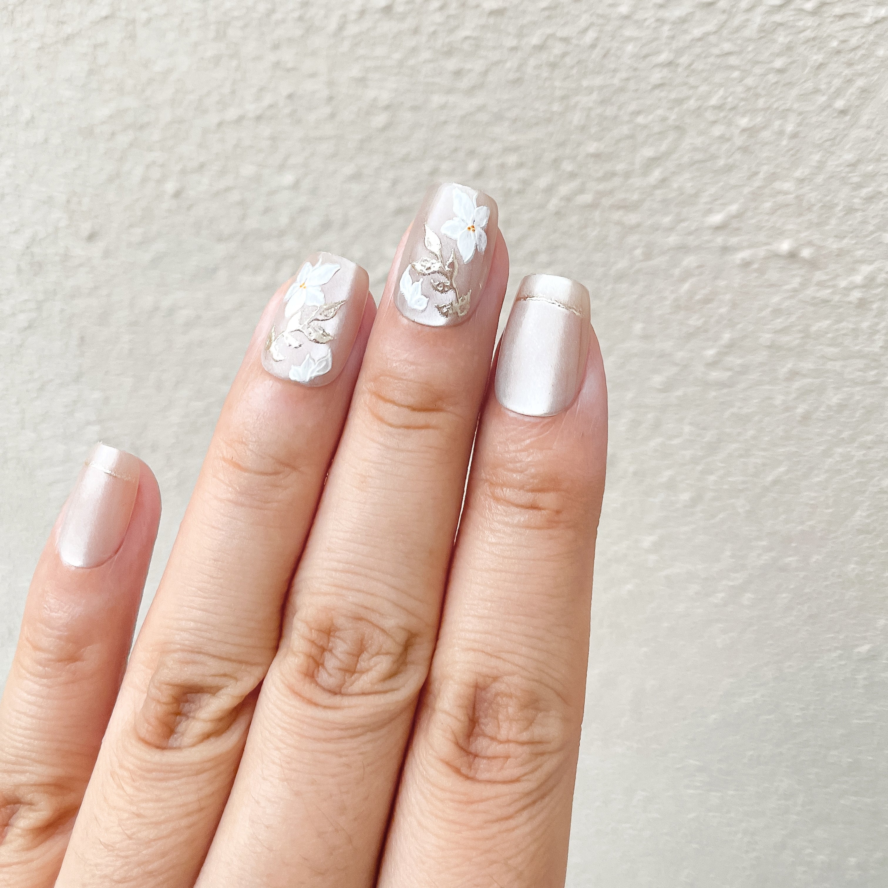 Close - up of fingers wearing ethereal floral embellished press - on nails with a soft pearl finish against a light background