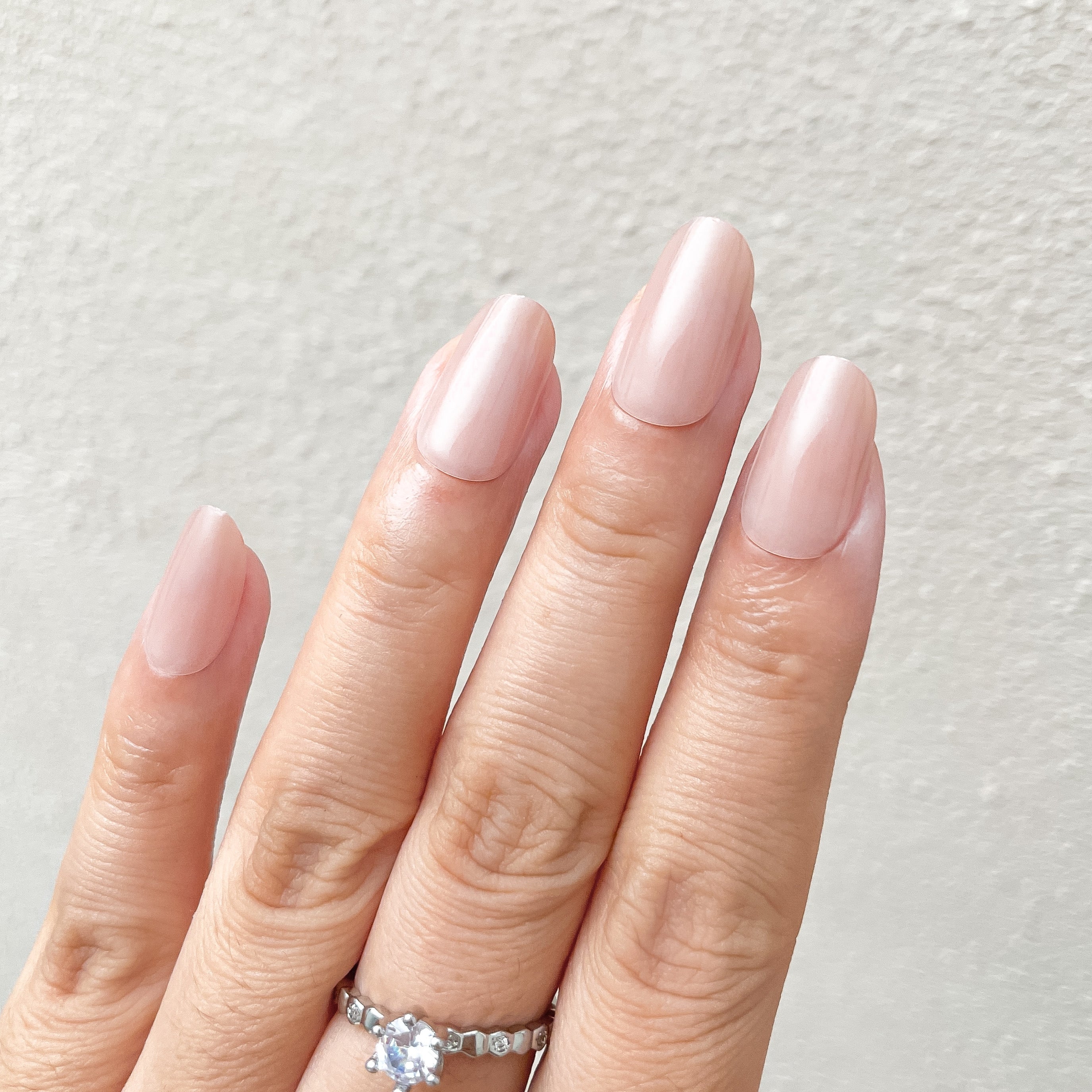 Hand with pink nail polish wearing a silver ring on a light gray background