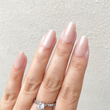 Hand with pink nail polish wearing a silver ring on a light gray background