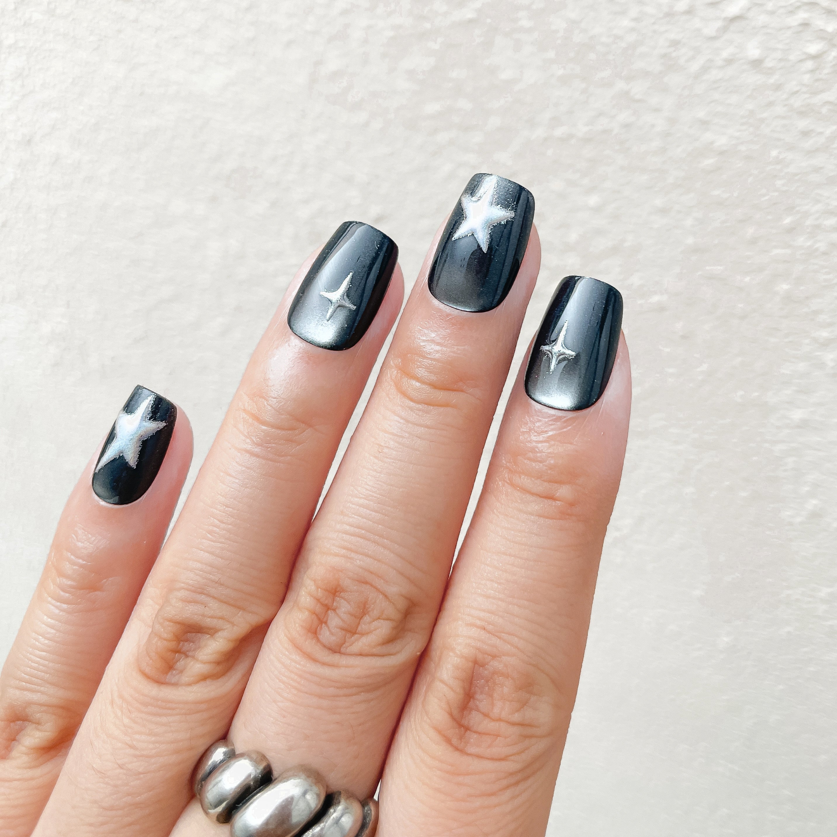 Hand with black nail polish featuring white star designs on a light background