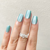 Close - up of fingers wearing mint green metallic press - on nails, featuring a unique silver textured ring against a light background