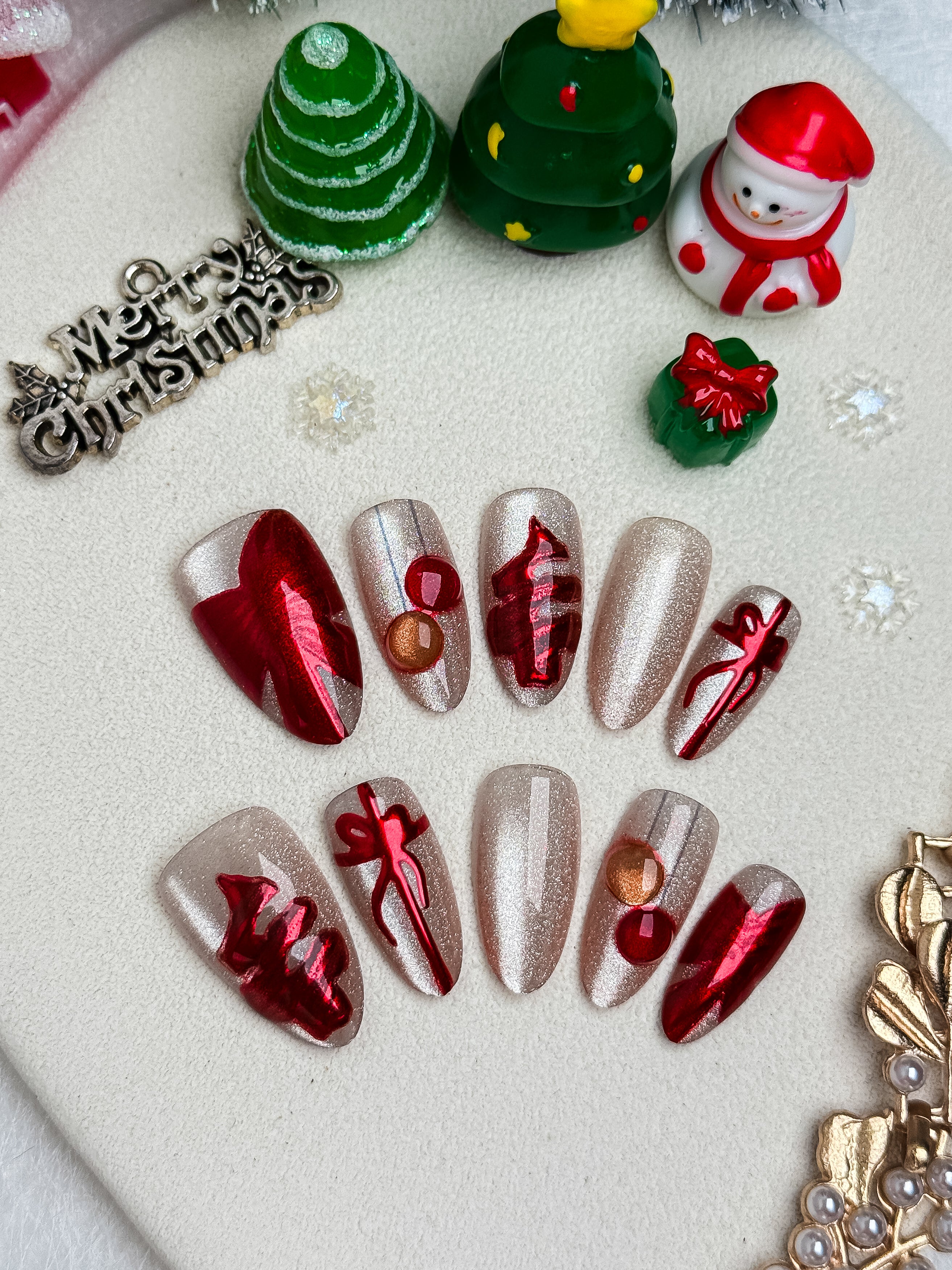 Christmas-themed nail art with red, silver, and gold decorations on a white background.