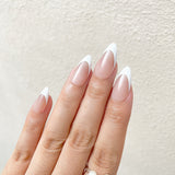 Close-up of a hand with almond-shaped nails painted in a gradient from beige to white on a neutral background.