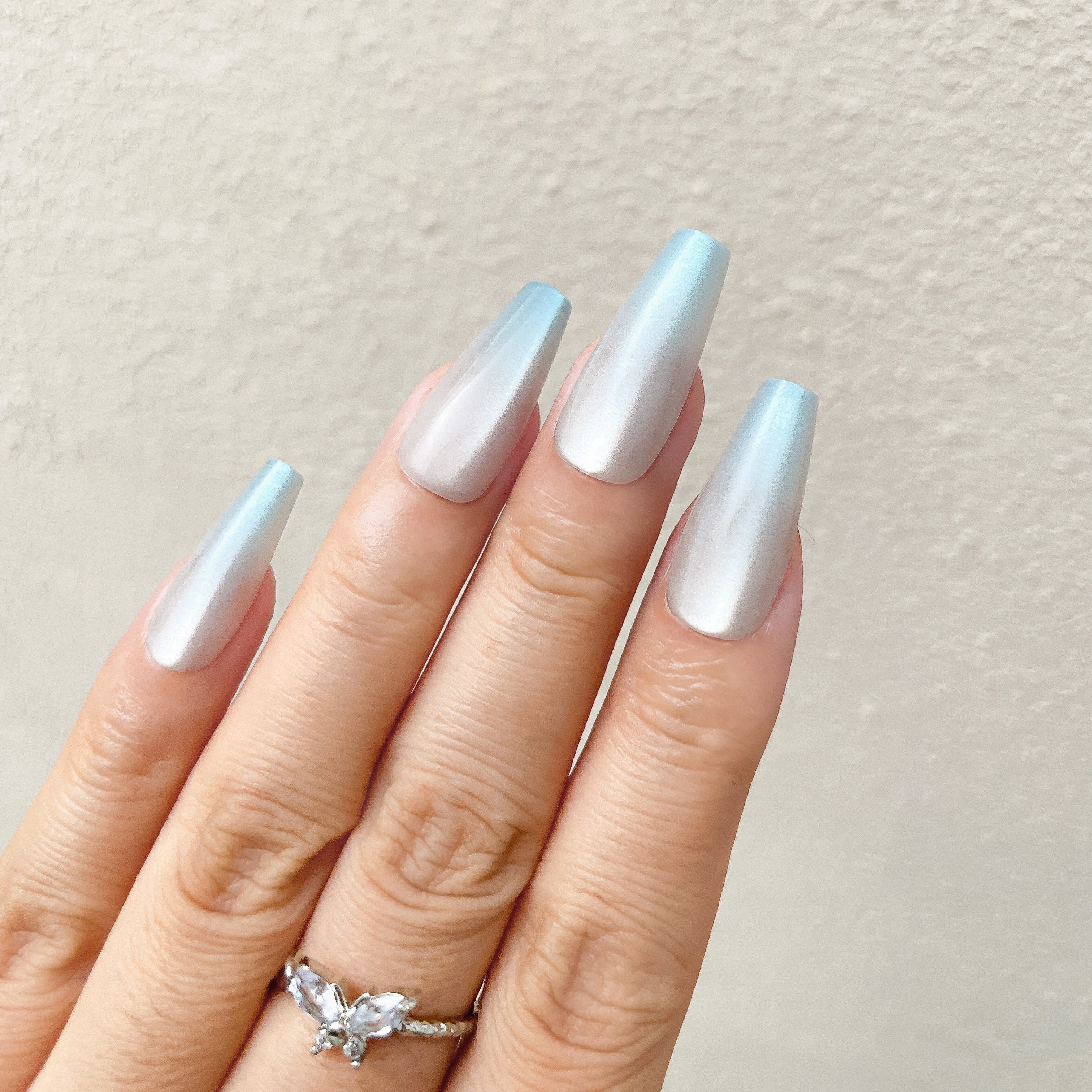 Close - up of fingers wearing blue - silver gradient stiletto press - on nails against a light background