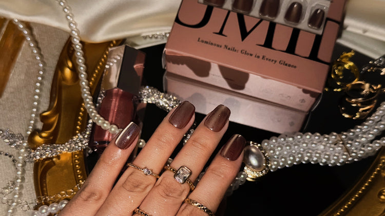 Manicured nails with dark polish, a box of nails, and jewelry on a decorative background